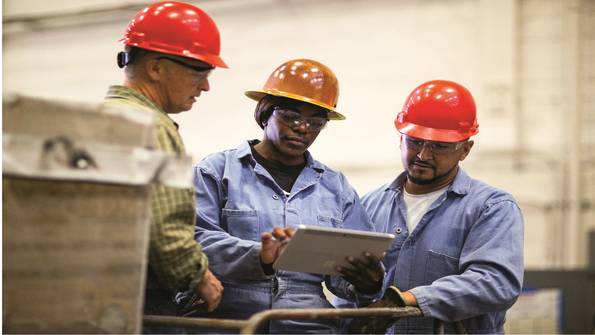 Three workers wearing hard hats look at a Microsoft Surface tablet