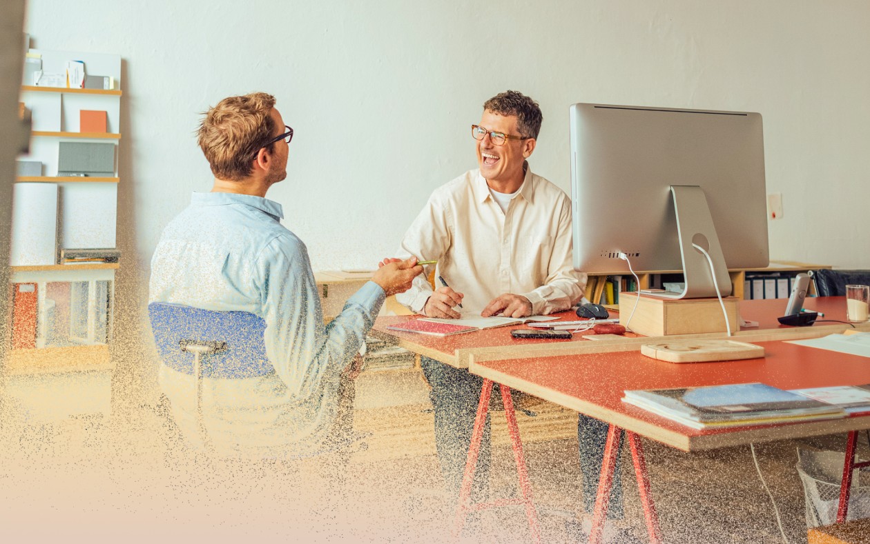 Two men sitting, talking and laughing in office