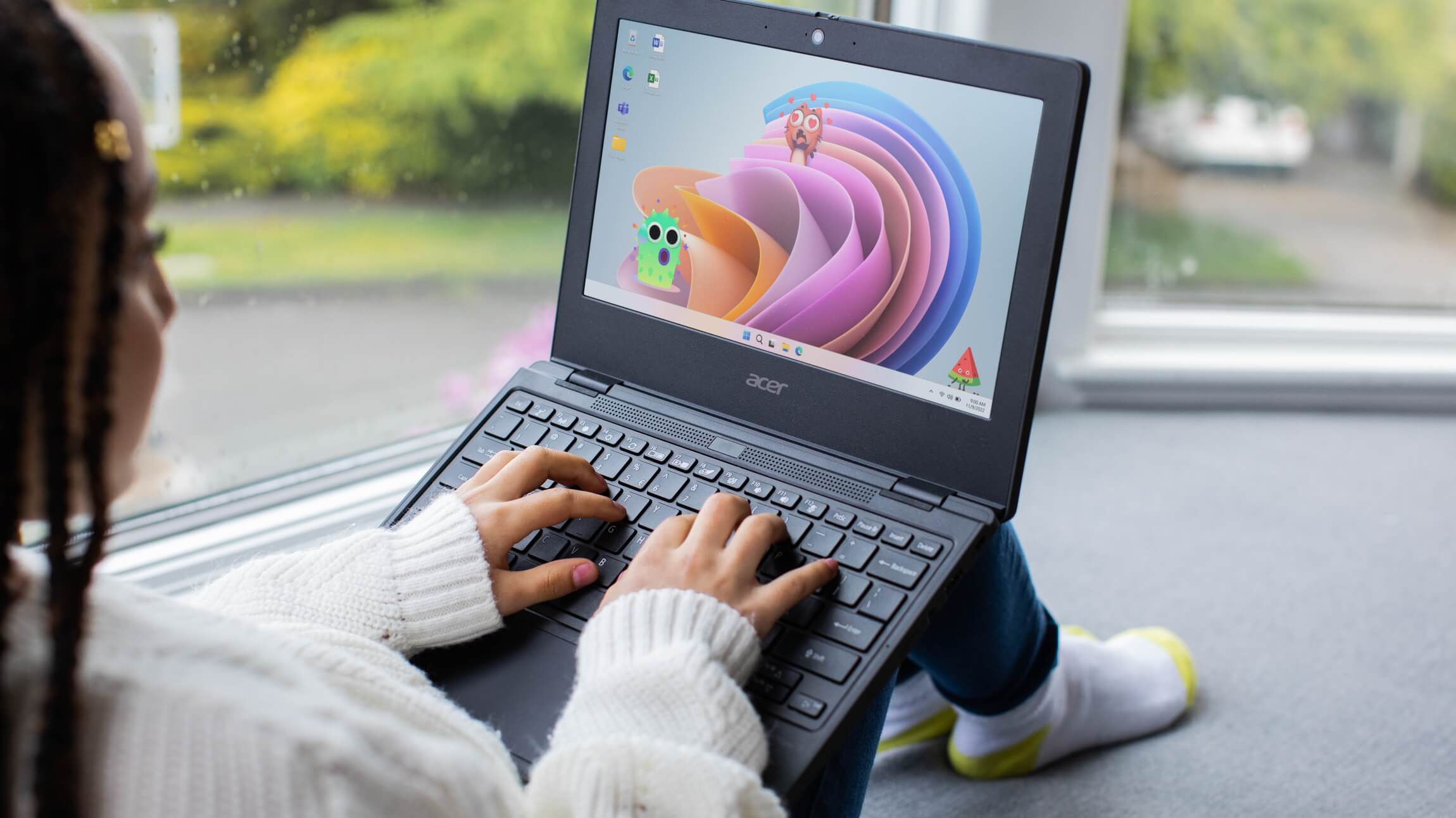 Female student sitting near windows at home and typing on a laptop in her lap.