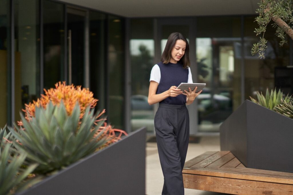 Uma mulher que participa de uma reuni&atilde;o do Microsoft Teams em seu tablet Surface enquanto caminha pelo p&aacute;tio externo de seu escrit&oacute;rio